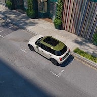 Overhead shot of a white car with an olive green roof parked on a sunny city street.