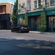 Black Mini Electric parked on a mostly empty street in front of a shop with a dark green facade.