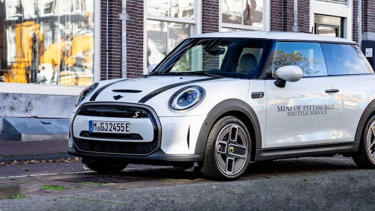 White Mini Cooper MINI OF PITTSBURGH SHUTTLE SERVICE parked on a street
with a brick building in the background