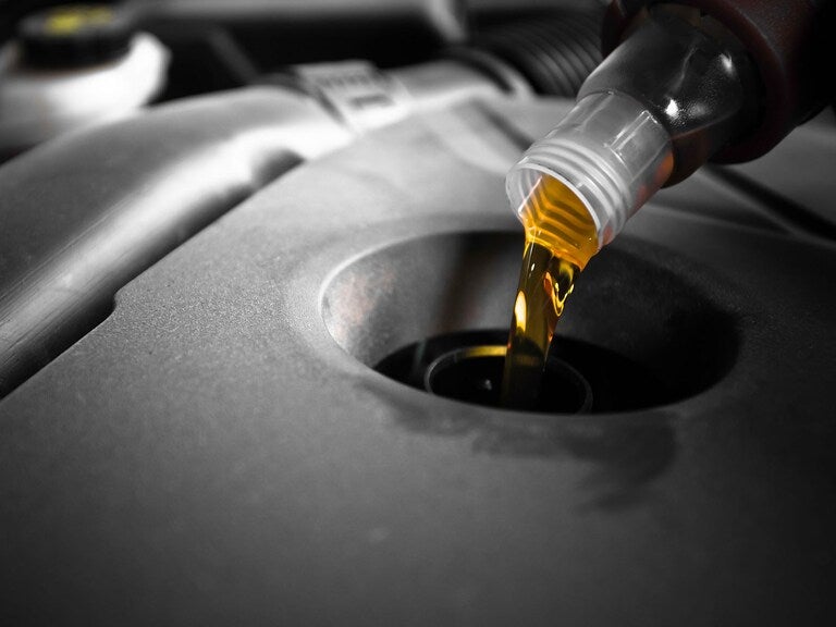 Golden yellow oil pouring from a clear plastic bottle into a dark engine compartment.